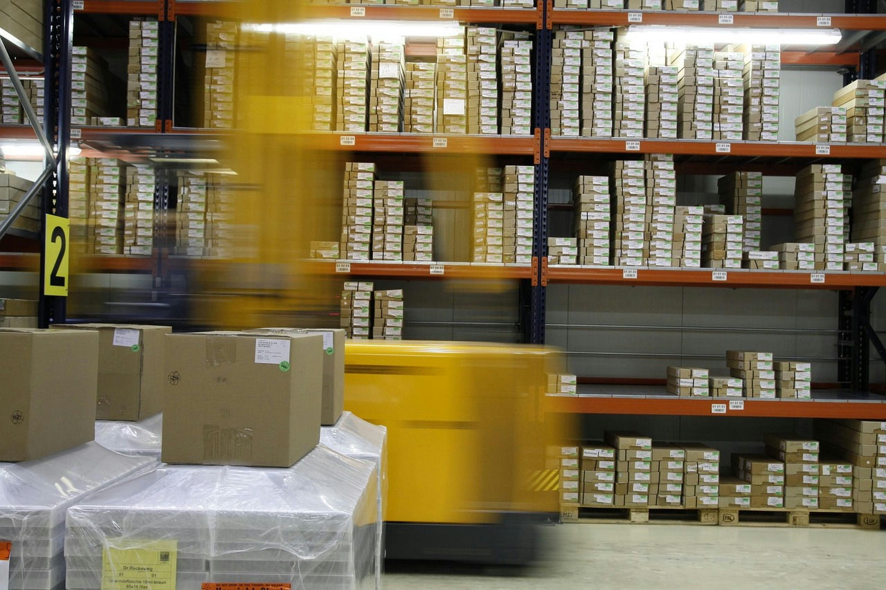 Warehouse racking with wrapped pallets of boxes and a forklift moving stock